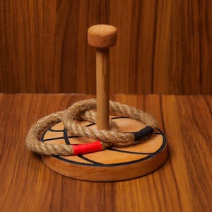Op de afbeelding: Een houten ringwerpspel met een bruine houten basis en een touwring. De basis is versierd met een zwart-wit basketbalontwerp.