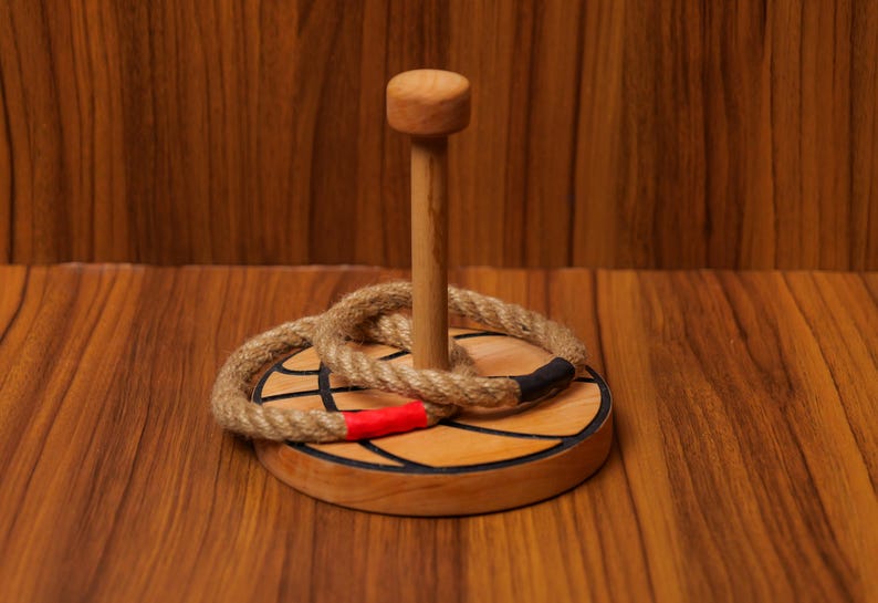 Op de afbeelding: Een houten ringwerpspel met een bruine houten basis en een touwring. De basis is versierd met een zwart-wit basketbalontwerp.