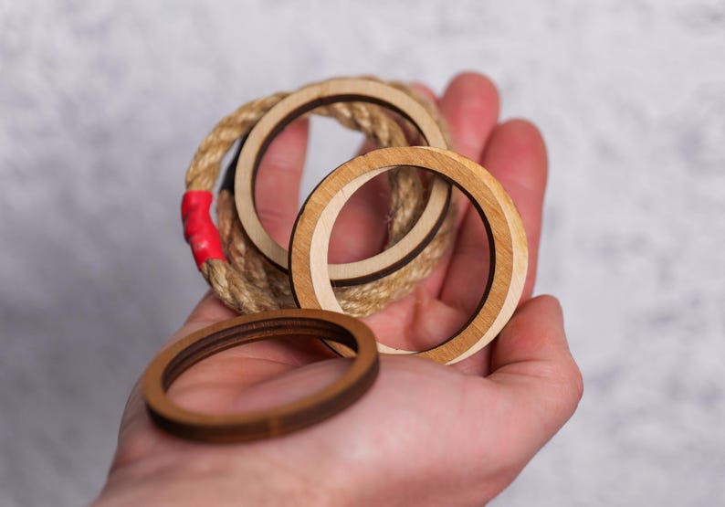 Op de afbeelding: Drie houten ringen, waarvan er &eacute;&eacute;n is omwikkeld met touw, vastgehouden in een hand. De ringen zijn van verschillende grootte en hebben een natuurlijke houten afwerking.