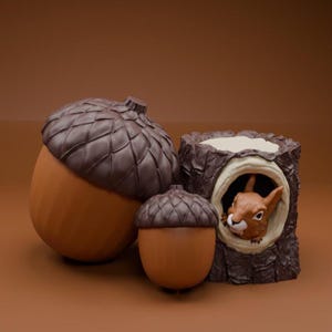 Pode incluir: Um arranjo caprichoso com dois recipientes em forma de bolota e uma floreira de tronco de árvore com um esquilo espreitando. As bolotas têm tampas castanhas e corpos laranja. O tronco é castanho com um esquilo dentro.