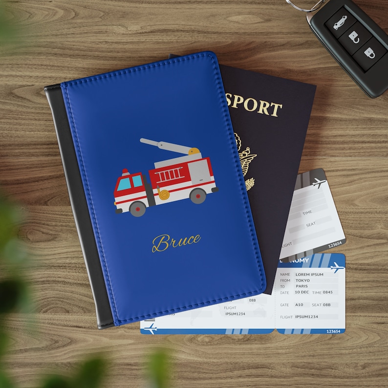 May include: A blue passport holder with a red fire truck illustration and the name "Bruce" printed in gold lettering. The holder is lying on top of a passport and boarding passes.