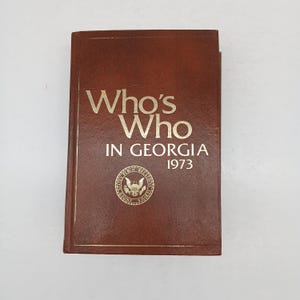May include: A brown leather-bound book titled "Who's Who in Georgia 1973" with a gold seal of the United States Public Health Service.