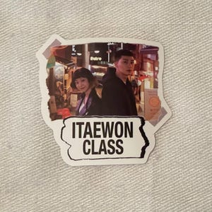 May include: A sticker featuring a photo of two people in a city setting. The text "ITAewon CLASS" is printed on the sticker.
