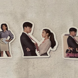 May include: Four stickers featuring characters from the Korean drama "Business Proposal". The stickers are printed on white paper with a glossy finish. The stickers feature the main characters in various scenes from the show.