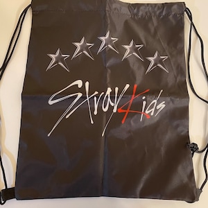May include: Black drawstring bag with a white "Stray Kids" logo and five silver stars.