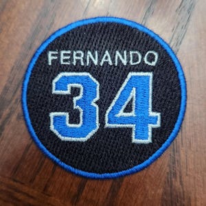 May include: A black and blue circular patch with the name "Fernando" and the number "34" in white.