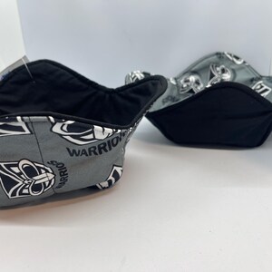 May include: Two black and grey fabric bowls with a pattern of a warrior's face and the word "WARRIORS" repeated. The bowls are lined with black fabric.