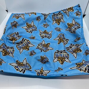 May include: A blue and gold fabric bowl with a repeating pattern of the Gold Coast Titans logo. The bowl is quilted and has a soft, plush texture.