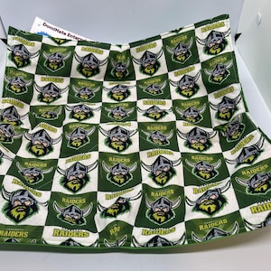 May include: A green and white checkered fabric with a repeated pattern of a green and gold viking helmet with the word "RAIDERS" printed on it.