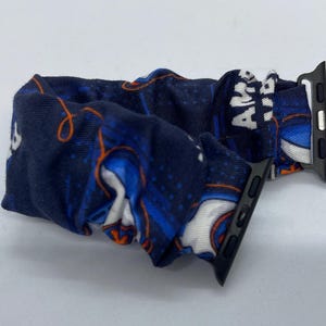 May include: A blue and white patterned Apple Watch band with a black metal clasp. The band has a design with orange and white accents and the word "AMERICA" printed on it.