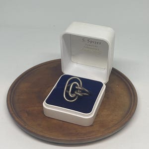May include: A silver ring with a unique, abstract design. The ring is in a white box with the text "S. Spijker Juwelier Amsterdam" on the top.