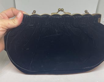 Może przedstawiać: Czarna aksamitna torebka typu clutch ze złotym zapięciem.