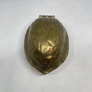 Könnte beinhalten: Ein Messingobjekt in Form einer Walnussschale mit einer strukturierten, unebenen Oberfläche und einem metallisch goldfarbenen Finish. Das Objekt verfügt über einen Klappmechanismus an der Oberseite zum Öffnen und hat eine abgerundete Form.