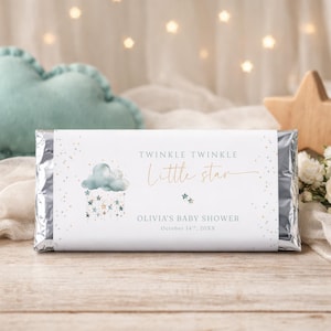 Peut inclure: Une barre chocolatée sur le thème d'une baby shower. L'étiquette porte l'inscription "Twinkle Twinkle Little Star" avec un motif de nuage et d'étoile. La date de la baby shower est imprimée en dessous. Un coussin en forme de nuage et une étoile en bois sont en arrière-plan.
