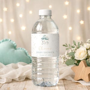 Peut inclure: Une bouteille d'eau en plastique transparent avec un bouchon blanc. L'étiquette présente un motif de nuage et d'étoiles avec le texte "Baby Shower Olivia". L'arrière-plan comprend une étoile en bois, des fleurs et un nuage bleu doux.