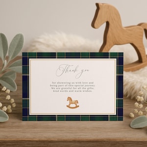 May include: A baby shower thank you card with a plaid border in navy blue, green, and gold. The card features the words "Thank you" in elegant script, along with a message and a rocking horse illustration. A wooden rocking horse is in the background.