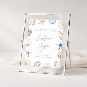 Peut inclure: Un panneau encadré sur le thème de la plage. Le panneau présente des illustrations à l'aquarelle de coquillages et d'étoiles de mer. Le texte sur le panneau indique "FULLY EDITABLE Custom Sign". Le cadre est en verre transparent et possède un support en métal argenté.