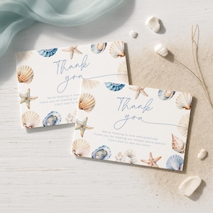 Puede incluir: Dos tarjetas blancas con temática de playa. Las tarjetas tienen las palabras "Thank you" en escritura azul. Están decoradas con conchas marinas, estrellas de mar y el texto "We're floating in love and gratitude. Thank you for making our shower extra special. Can't wait to see you soon!"