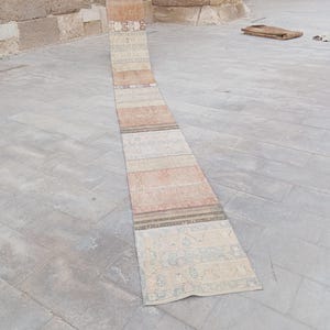 Puede incluir: Una alfombra de pasillo larga y estrecha con un diseño de patchwork de varias secciones rectangulares. La alfombra presenta una paleta de colores suaves en beige, tostado, azul claro y naranja desteñido, con patrones geométricos y florales.