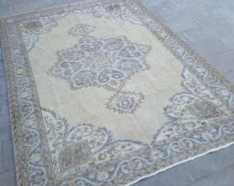 May include: A rectangular beige rug with an intricate floral pattern in shades of blue, brown, and cream. The rug features a detailed border and a central medallion design. The rug is placed on a gray stone surface.