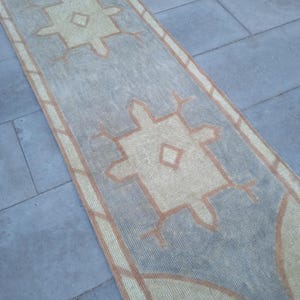 May include: A light blue and beige runner rug with a geometric pattern. The rug has a distressed look and is made of a woven material.