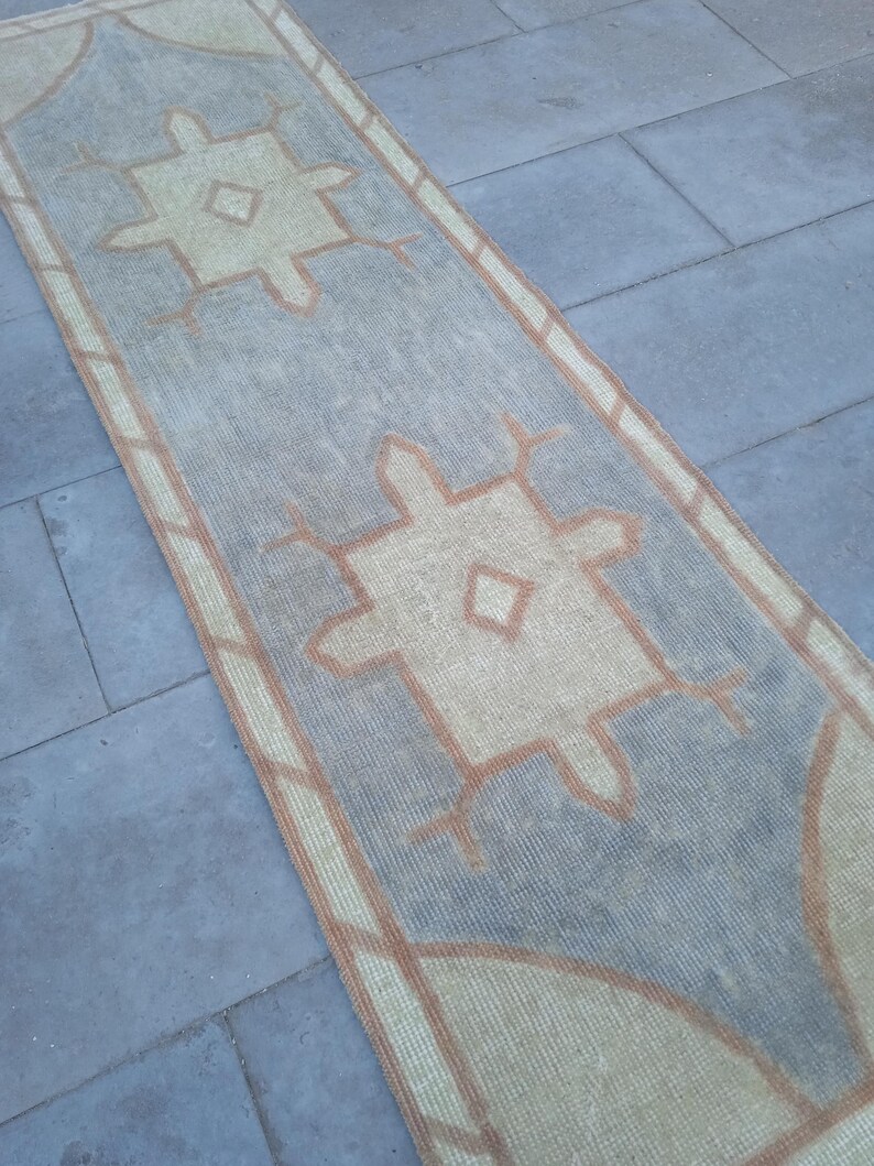 May include: A light blue and beige runner rug with a geometric pattern. The rug has a distressed look and is made of a woven material.