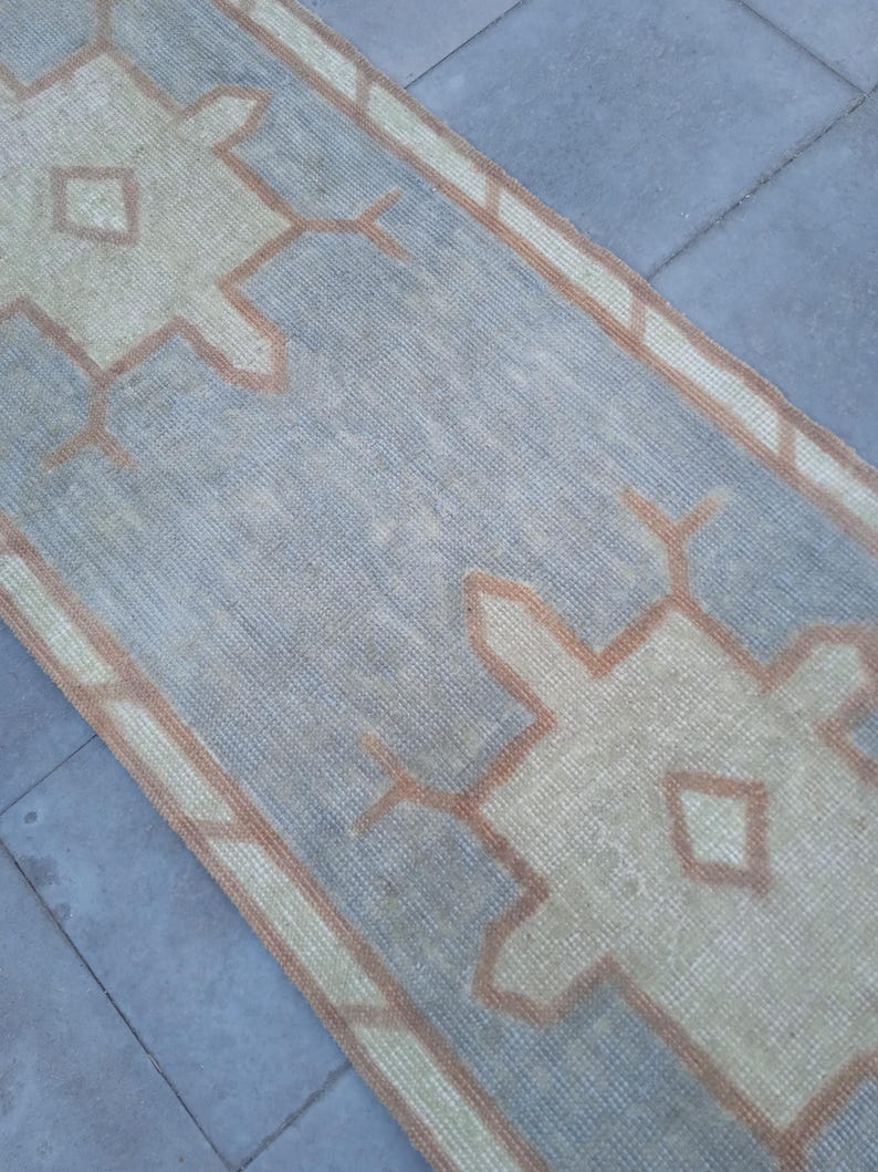 May include: A light blue and beige runner rug with a geometric pattern. The rug has a faded look and is made of a woven material.