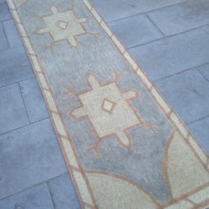 May include: A long, rectangular rug with a light gray background and a beige and brown geometric pattern. The rug has a fringed edge.