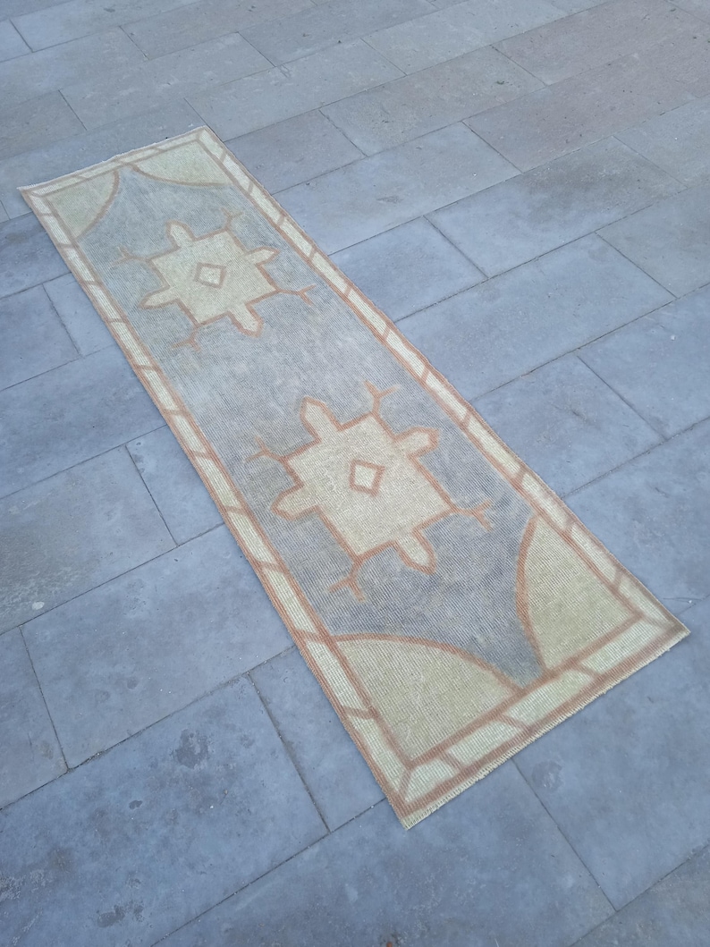 May include: A long, rectangular rug with a geometric pattern in shades of beige and brown. The rug has a faded, vintage look and is perfect for adding a touch of bohemian style to any room.