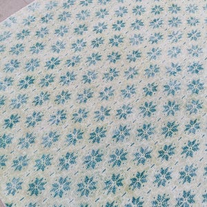 以下が含まれることがあります： クリーム色の背景に、ターコイズブルーの花柄が繰り返されるヴィンテージスタイルのラグ。 ラグは使い古されたような外観で、アンティークまたは使い古された美学を持つ複製である可能性があります。 デザインは対称的で、表面全体をカバーしています。