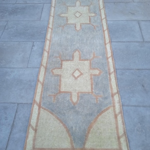 May include: A long, rectangular rug with a geometric pattern in shades of beige, brown, and gray. The rug has a fringed edge and features a repeating design of stylized stars.