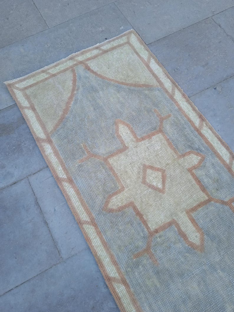 May include: A light blue and beige runner rug with a geometric pattern. The rug has a brown border.