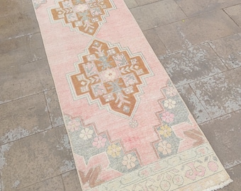 May include: A rectangular, vintage-style runner rug with a pink background and geometric patterns in shades of brown, gray, and cream. The rug features floral and ornamental designs, with a fringed edge.