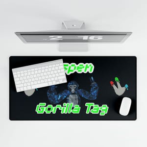 May include: A black rectangular desk mat featuring a central blue gorilla graphic, the green pixelated text "Gorilla Tag" below, and a grey handprint with red, green, and blue paint drips on the right side. The mat is positioned under a white keyboard.