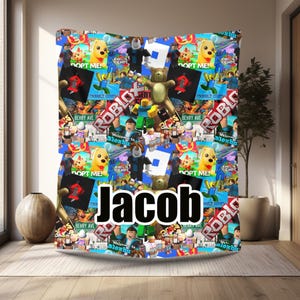 Pode incluir: Um cobertor colorido com uma colagem de personagens, logotipos e frases do jogo Roblox. O cobertor tem um padrão repetitivo com imagens de cães, ursos e personagens. O nome "Jacob" é exibido em letras brancas grandes.