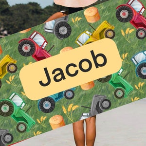 May include: A green, yellow, and red tractor pattern beach towel with the name Jacob printed on a yellow label.