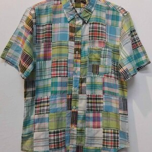 May include: A short-sleeved button-down shirt with a patchwork design. The shirt features a variety of plaid patterns in shades of blue, green, yellow, pink, and red. It has a button-down collar and a chest pocket.