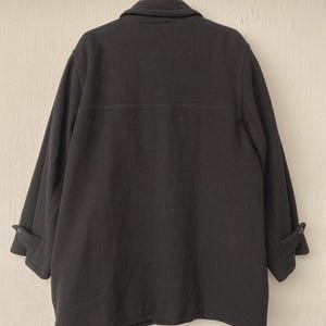 May include: A black wool coat with a button-down front and a collar, hanging on a red hanger. The coat has long sleeves with buttoned cuffs. The back of the coat is visible, showing a simple, classic design.