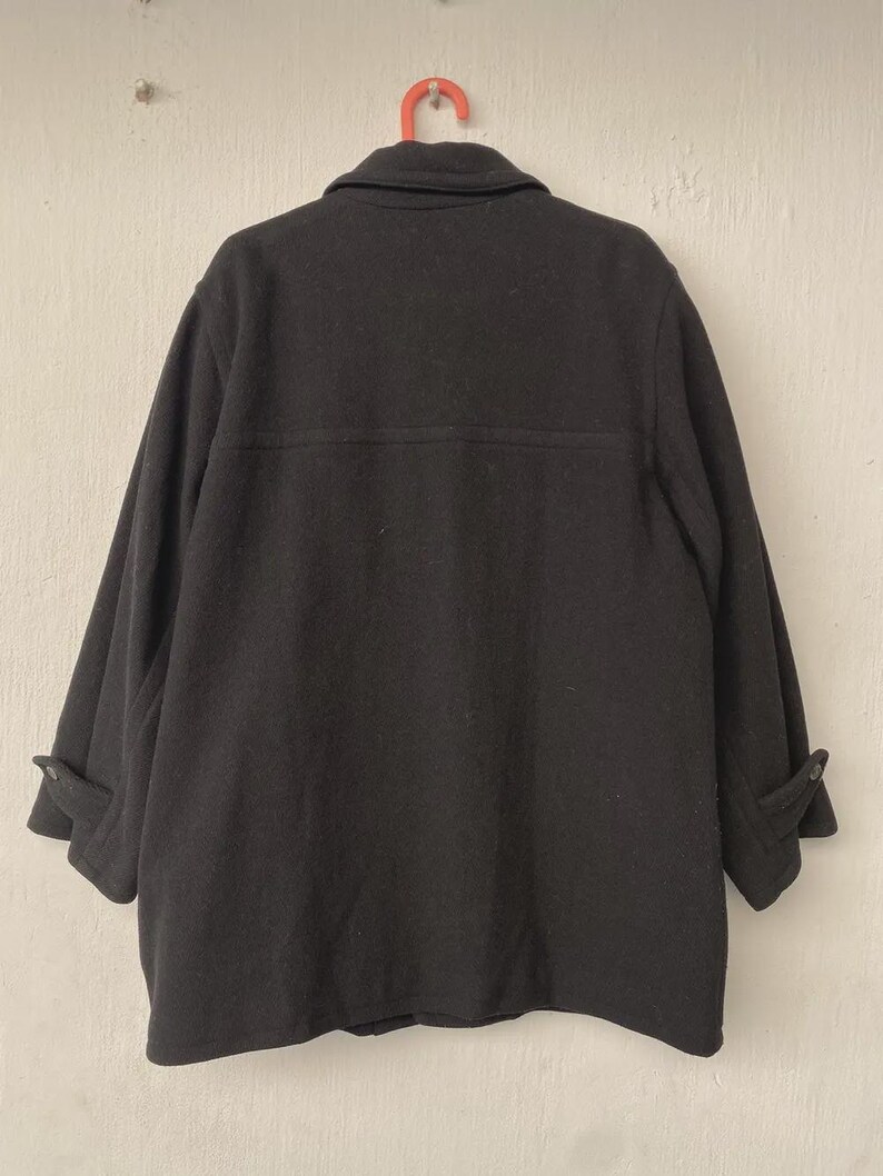 May include: A black wool coat with a button-down front and a collar, hanging on a red hanger. The coat has long sleeves with buttoned cuffs. The back of the coat is visible, showing a simple, classic design.