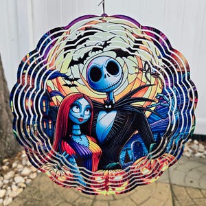 Puede incluir: Un molinillo de viento de metal de m&uacute;ltiples capas con Jack Skellington y Sally de Pesadilla antes de Navidad. El dise&ntilde;o es una ilustraci&oacute;n colorida y detallada de los personajes sobre un fondo de una escena de Halloween espeluznante.
