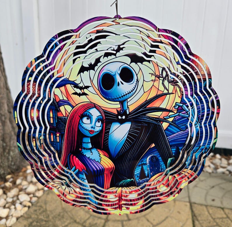 Puede incluir: Un molinillo de viento de metal de m&uacute;ltiples capas con Jack Skellington y Sally de Pesadilla antes de Navidad. El dise&ntilde;o es una ilustraci&oacute;n colorida y detallada de los personajes sobre un fondo de una escena de Halloween espeluznante.