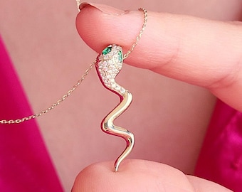 May include: A gold snake necklace with green gem eyes. The snake is coiled and has a diamond-like pattern.