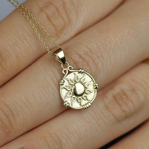 May include: A gold necklace with a sun pendant. The pendant is round and has a detailed design of a sun with rays.