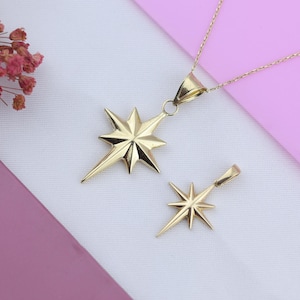 May include: Two gold star-shaped pendants on a white background. The larger pendant is on a chain and the smaller pendant is on a separate chain.