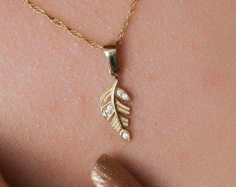 May include: A delicate gold necklace with a small leaf pendant accented with tiny clear stones.