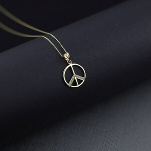 May include: A gold peace sign pendant necklace with small clear stones around the edges. The necklace is on a black surface.