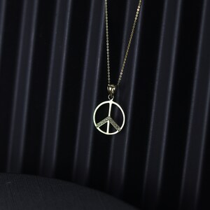 May include: A gold peace sign pendant necklace with small clear stones set in the peace sign.