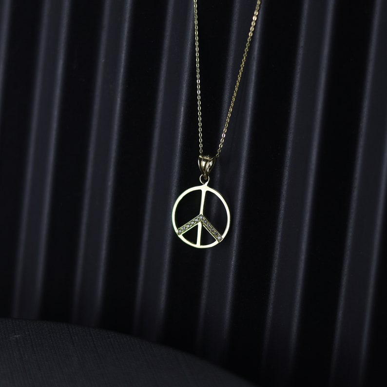May include: A gold peace sign pendant necklace with small clear stones set in the peace sign.