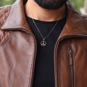 May include: A man wearing a brown leather jacket with a zipper and a gold peace sign necklace.