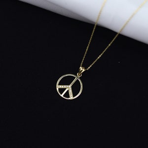 May include: A gold peace sign pendant necklace with small clear stones around the edge. The necklace is on a black background.
